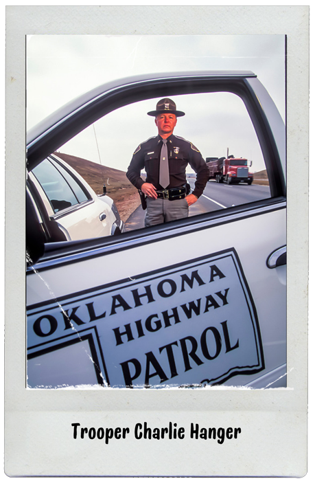Trooper Charlie Hanger of the Oklahoma Highway Patrol. Is standing next to his patrol car.